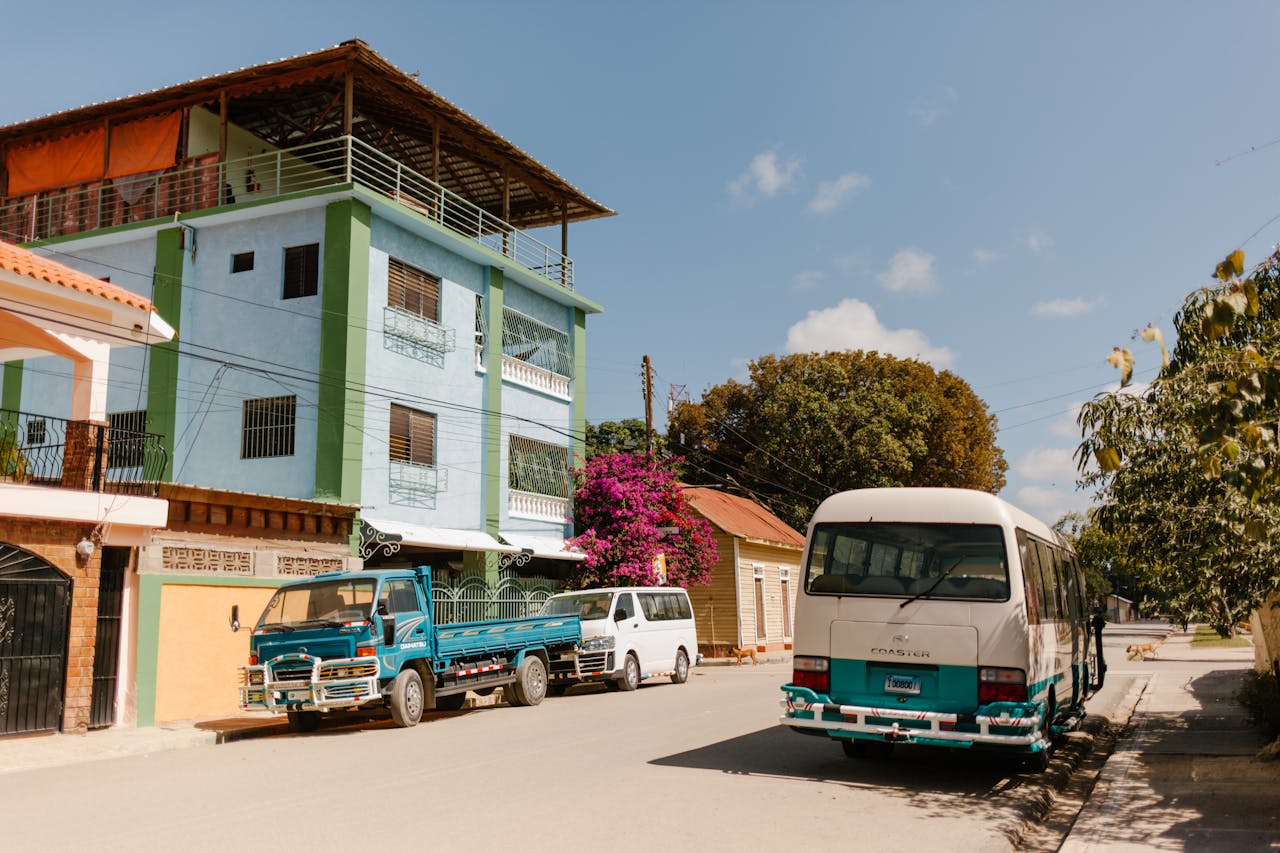 Bright sunny street with colorful buildings and parked vehicles in a Dominican Republic town.